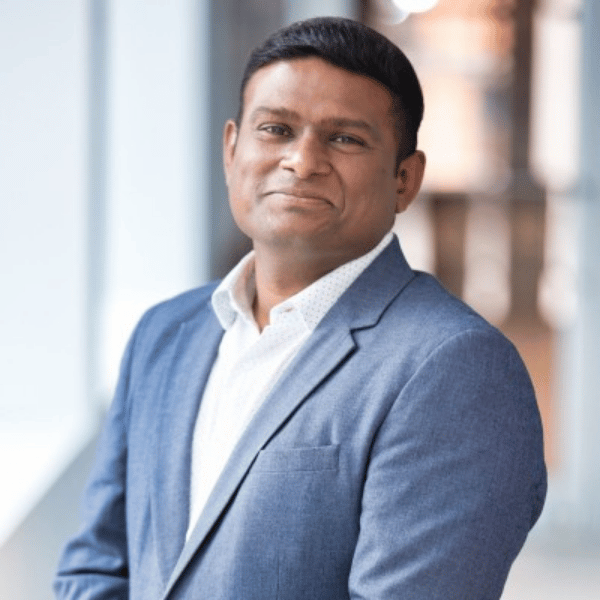 Manish’s headshot shows him in a light‑blue blazer and white shirt, smiling slightly.