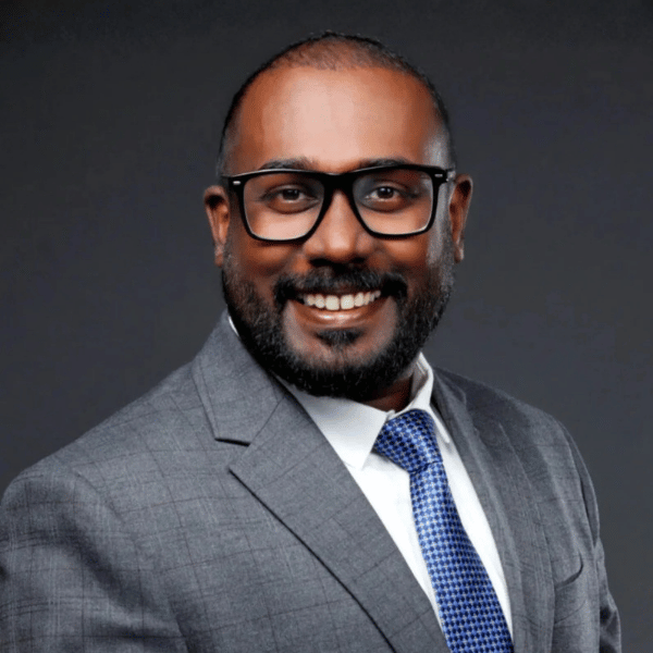 Nithin’s headshot, smiling in a gray suit with a white shirt and a blue striped tie, wearing black‑rimmed glasses.