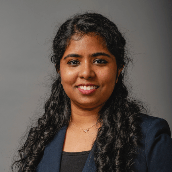 Reshma’s headshot features long, curly dark hair, a dark blazer, and a top.