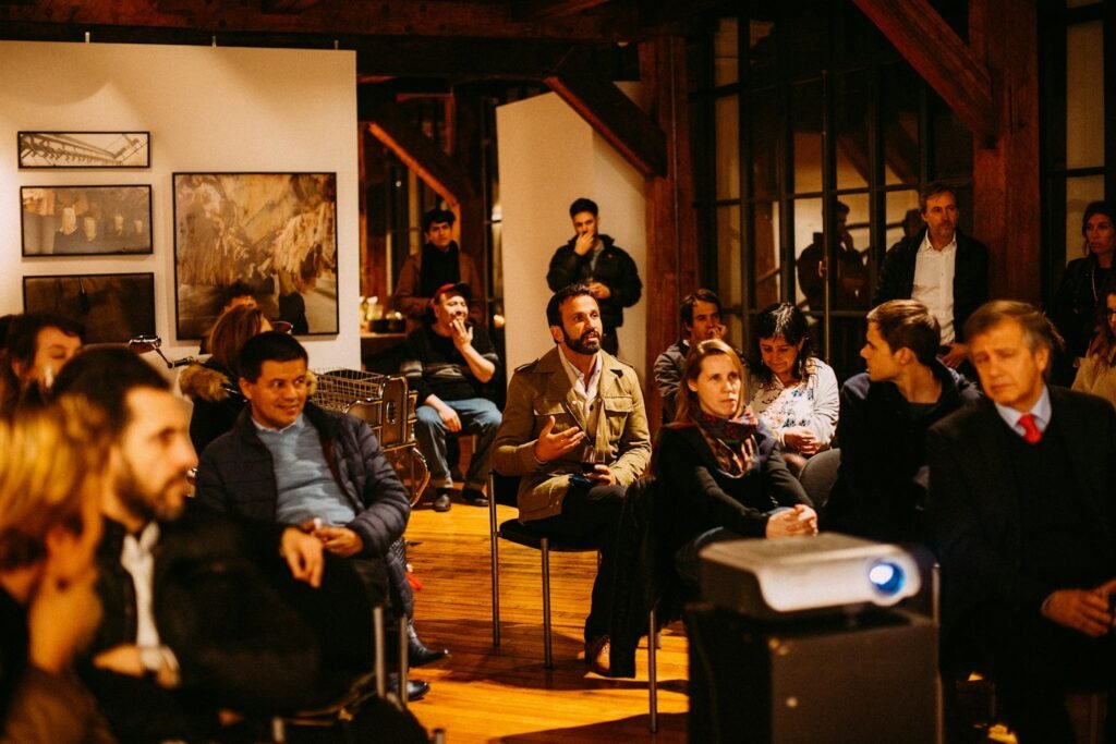 An audience listening to a speaker in a warmly lit room